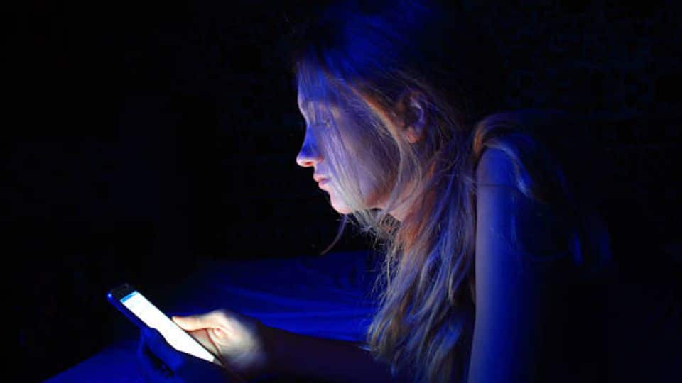 Teenager In Dark Room Looking At Phone With High Brightness